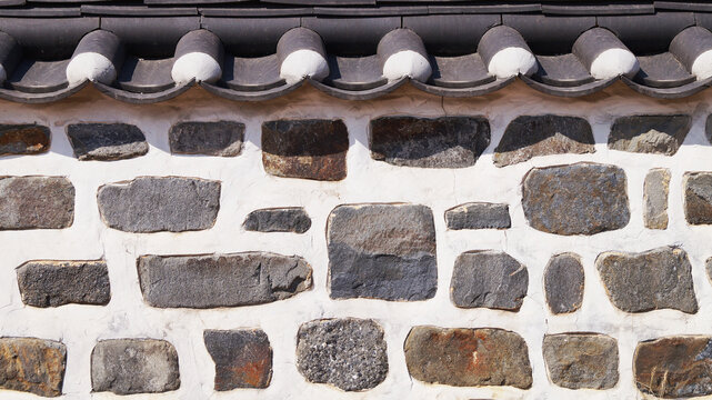 Close-up of a traditional Korean stone wall with a Hanok tiled roof. Ideal as a cultural background, architectural texture, heritage concept, and traditional Korean design element.