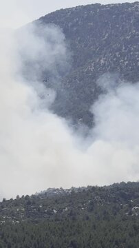 High-angle view of a firefighting helicopter navigating fierce flames and heavy smoke during an emergency forest mission