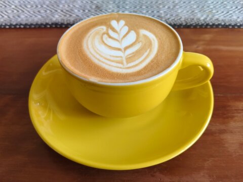Yellow Ceramic Cup of Latte with Rosetta Art on Wooden Table in Cafe