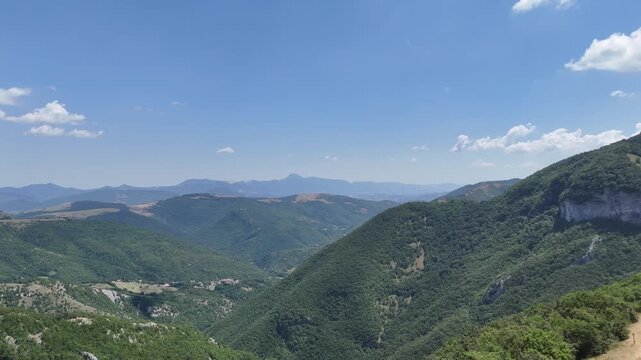 Catena montuosa con colline verdi, vallate profonde e vegetazione fitta che si estende verso l&rsquo;orizzonte sotto un cielo azzurro con leggere nuvole. Paesaggio naturale ampio, luminoso e incontaminato
