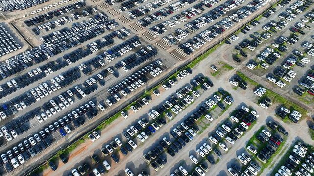 High-angle aerial view of thousands of new cars arranged in organized rows, showcasing automotive industry scale, production capacity, inventory control, and data-driven logistics systems. 4k.
