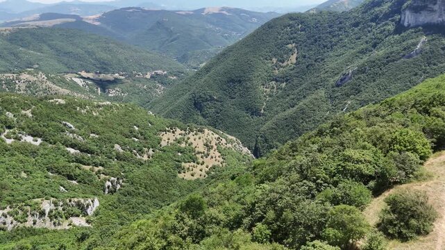 Montagne verdi con pendii ripidi, vallate profonde e vegetazione fitta che si estende fino all&rsquo;orizzonte sotto un cielo limpido. Paesaggio naturale vasto e incontaminato