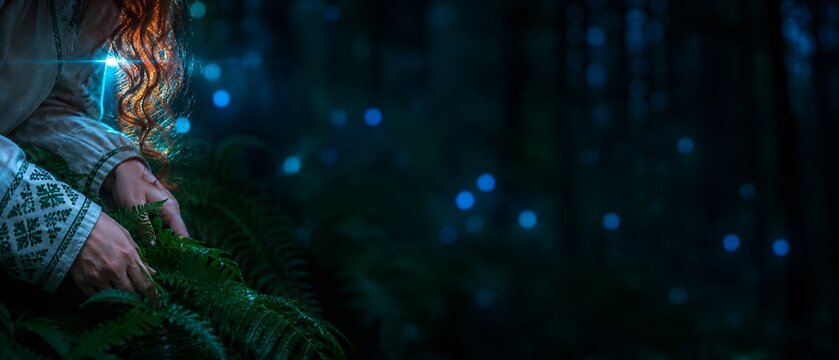 Close up of young redhead woman hands touching fern leaves in mystical dark forest with glowing lights on midsummer night, folklore magic concept with copy space