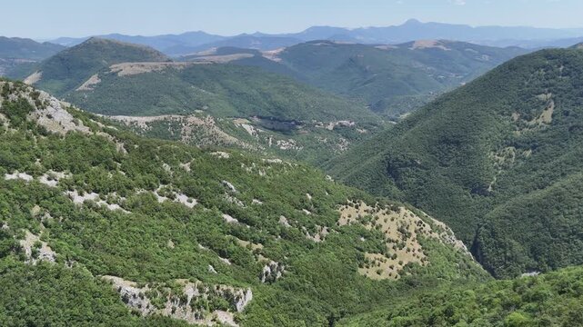 Catena montuosa con vallate verdi e pendii rocciosi sotto un cielo azzurro, in un paesaggio naturale vasto e incontaminato