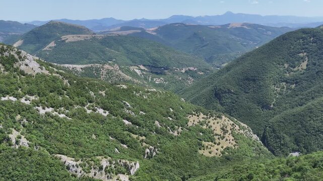 Catena montuosa con vallate verdi e pendii rocciosi sotto un cielo azzurro, in un paesaggio naturale vasto e incontaminato