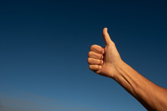 Hand showing thumbs up gesture against sky
