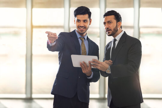 Corporate employees in formal business suit holding a tablet,with one of them showing something to other with his finger.