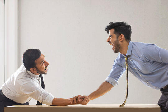 Corporate employees in formal clothing engaged in an arm wrestling match with one of them defeated.