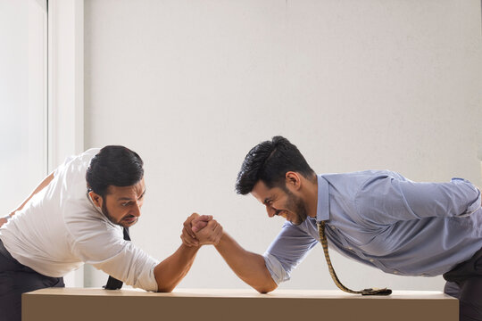 Corporate employees in formal clothing engaged in an arm wrestling match with one of them about to lose.