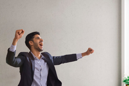 Portrait of a corporate employee in formal business suit clenching fists to celebrate his success.