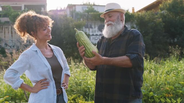 Senior farmer proudly showing a large zucchini to a woman