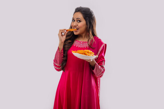 Indian woman in pink salwar eating Jalebi on festival
