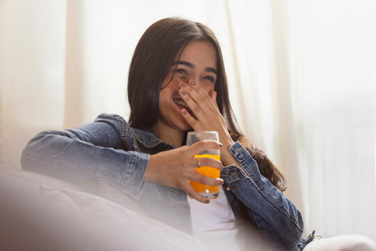 Young girl with a glass of juice smiling with covering her mouth