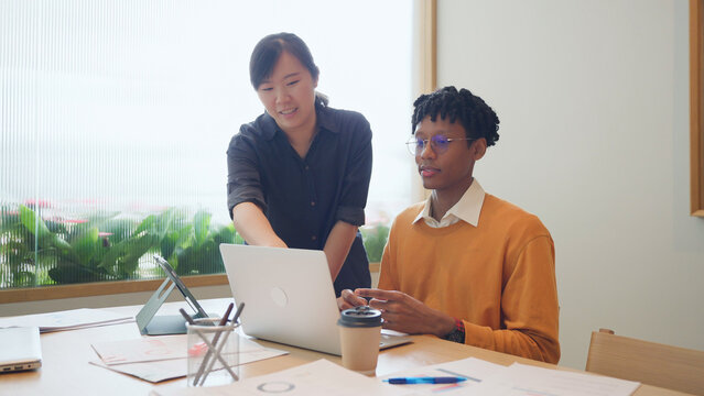 Diverse young colleagues working together on laptop computer in modern office, business collaboration concept
