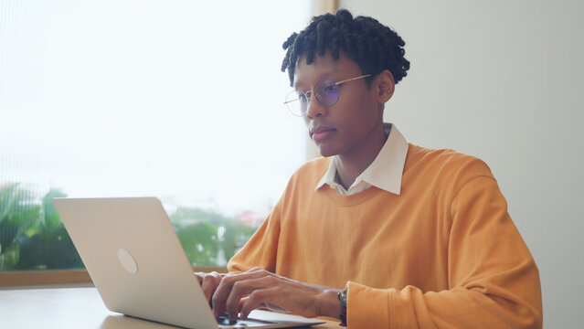 Focused young black man typing on laptop while working remotely in bright modern office.	