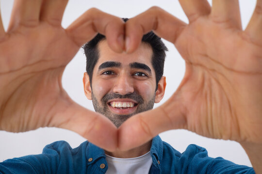 Adult man forming heart shape with her fingers and looking at camera through it
