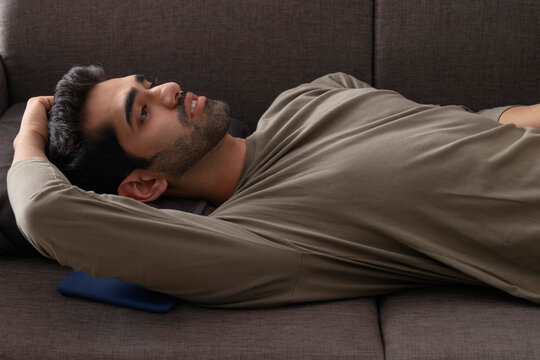 Portrait of a young man lying on sofa with a Smartphone kept beside 
