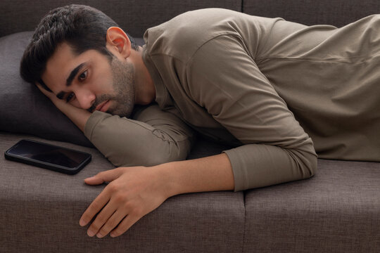 Portrait of a young man lying on sofa with a Smartphone kept beside 