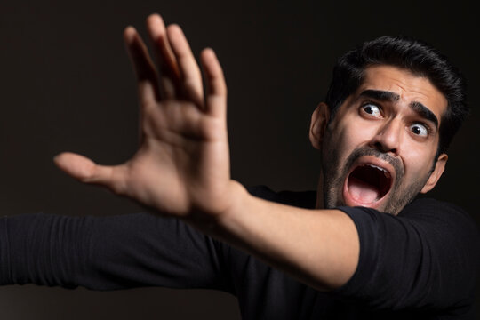 Portrait of a frightened young man looking away,raising hand and shouting 