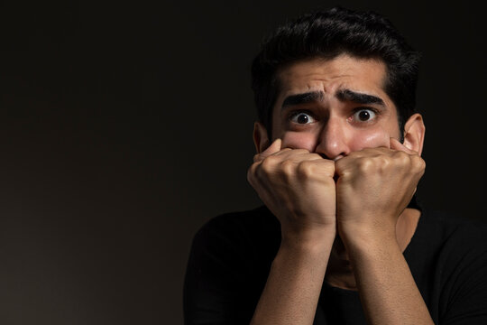 Portrait of a frightened young man looking  with big eyes and holding face with his hands
