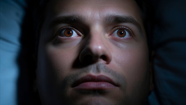 Caucasian man patient lying awake in bed at night with eyes wide open for sleeplessness and sleep disorder awareness