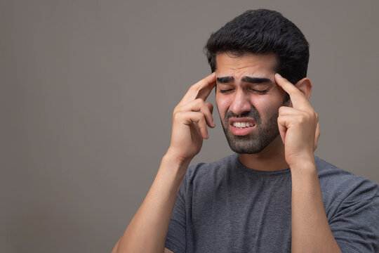 Portrait of a young man suffering from headache with hands on forehead 