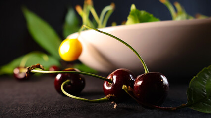 Ripe dark red cherries featuring a bright yellow cherry and fresh green leaves creating a vibrant contrast, with a blurred white bowl in the soft background, highlighting healthy eating © Dark Artistic