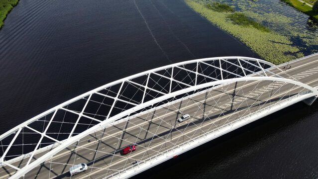 Modern Parnu Raama bridge connecting urban landscapes over a river filled with green duckweed and waterlilies, featuring cars driving on its asphalt surface