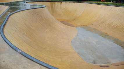 Obraz premium Concrete skatepark bowl showcasing its empty, curved interior with wet surfaces and metal coping, reflecting the aftermath of a rainy day in an outdoor urban sports zone