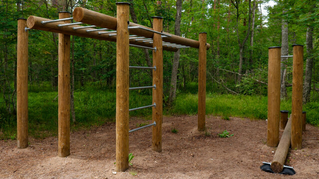 Outdoor calisthenics gym featuring wooden posts and metal bars for fitness training, blending seamlessly with the surrounding tranquil forest environment and natural setting