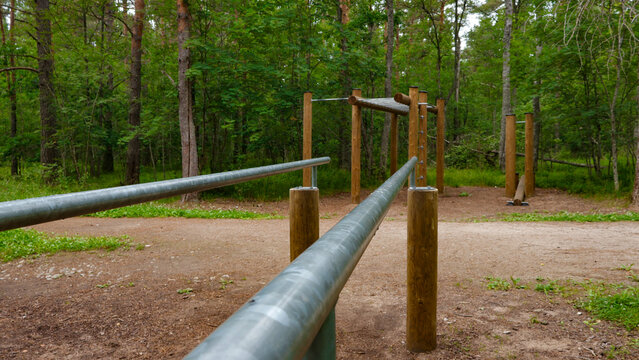 Outdoor gym space with parallel bars, pull up bars, and various wooden training elements, offering a natural environment for fitness and health activities