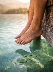 Fototapeta premium Close Up of Feet Dangling Off Wooden Dock Into Crystal Clear Lake