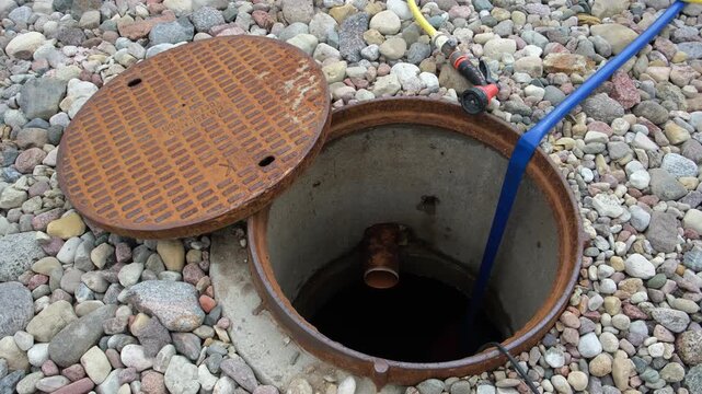 An open sewer manhole. A service cleaning of blocked sewer. A concrete septic tank with a plastic pipe. Rinse and pumping water out. Maintenance work, utility service, underground infrastructure. 4k.