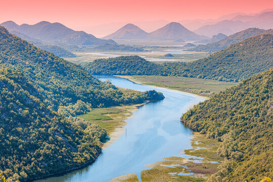Serpentine Crnojevic river flowing through a lush green valley in Montenegro, surrounded by rolling hills under a vibrant sunset sky in Skadar lake park