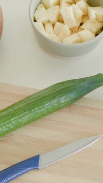 Vertical video: Panning camera showing cucumber on board, paring knife sliding, bowl revealing prep
