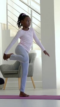 Vertical video: Practicing from arms-up kid in activewear balancing on purple mat home holding foot