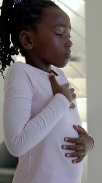 Vertical video: Practicing calming breaths girl in pink top with hands on chest near couch, stairs