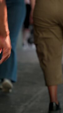 Vertical video: Entering frame, person in tan shorts leading group along passage to exit with purse
