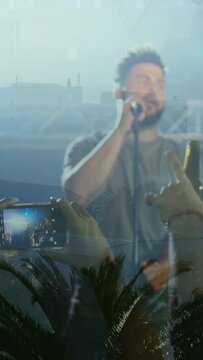 Vertical video: Music fan raising phone filming while singer singing into mic, crowd raising hands