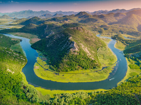 Rijeka Crnojevica river forming a striking horseshoe bend from an aerial view, surrounded by green mountains and lush vegetation in Skadar park, Montenegro