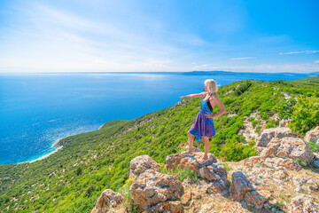 Obraz premium Woman in a colorful dress and hat enjoying the panoramic view of the historic Lubenice village on Sveti Ivan Lubenice Beach. A medieval settlement on Cres Island. Croatia of Cres Island in Croatia