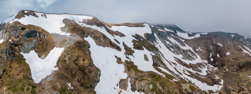 Mountain ranges showing melting snow patches on rocky terrain and greening slopes, signaling the changing seasons and nature