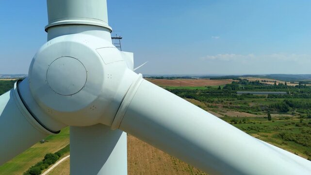 Close-up aerial orbit shot tracking around the industrial nacelle and hub assembly of a massive wind turbine generating clean energy.