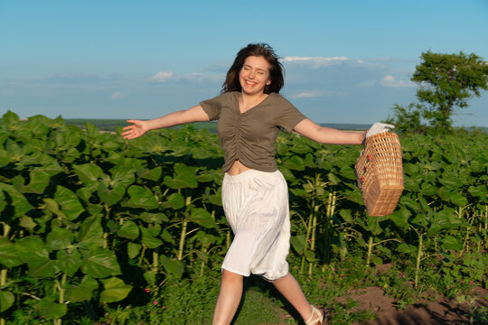 Happy young woman running through sunflower field with basket
