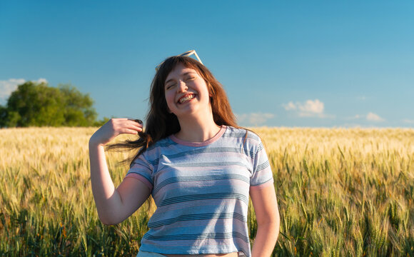 Happy young girl laughing in a golden wheat field during summer sunset