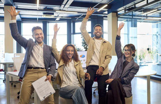 Team colleagues celebrate success with cheerful applause. Diverse coworkers in a modern office raise hands, cheering after meeting goals and marking a celebration. Teamwork and success concept.