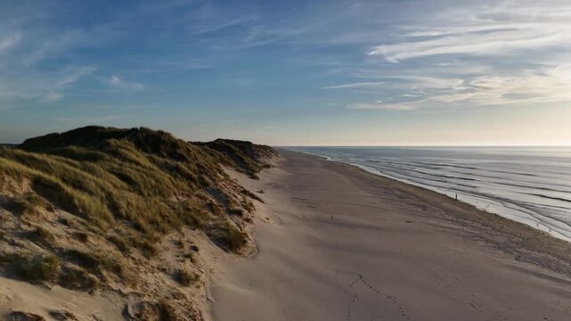 Evening aerial showing beach walkers and dune crests.