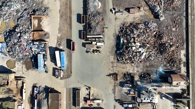 Direct overhead drone view of a large scrapyard with sorted metal piles industrial textures and a moving truck.