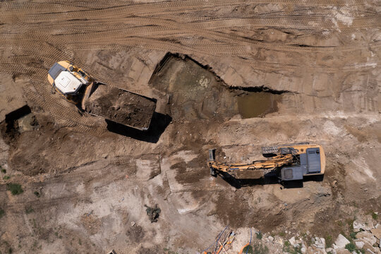 Excavator and dump truck performing earthmoving work at construction site aerial view