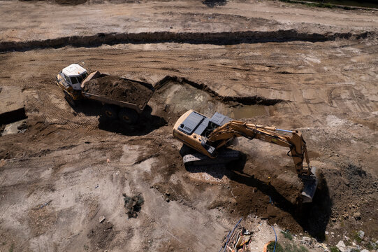 Excavator and dump truck performing earthmoving work at construction site aerial view